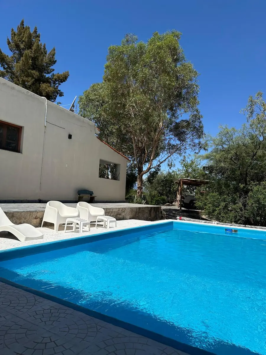 Piscina de una casa de campo en El Pedregal, con la casa y los árboles de fondo